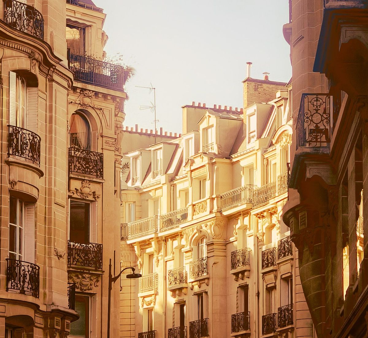 A Parisian street in warm evening light, lined with classic stone apartment buildings and wrought-iron balconies.